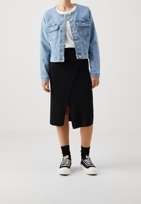 Person wearing light blue denim jacket, white shirt, black wrap skirt, black socks, and black high-top sneakers with white soles.