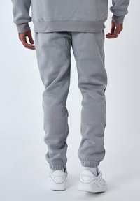 Pantalones de chándal grises hechos de una tela suave con una cinturilla y puños elásticos, combinados con zapatillas blancas. Detalles de costura visibles.