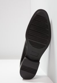 Semelle de chaussure habillée noire avec grip texturé et taille 42 marquée, inclinée sur un fond d'angle blanc.
