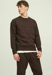 Bruin fleece sweatshirt met een ronde hals, zachte textuur en geribbelde boorden. Gedeeltelijk gedragen met een witte gelaagde shirt eronder.