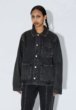 Tummansininen farkkutakki rentouttavalla leikkauksella, jossa on kaulus, etutaskut ja hopeiset nepparit. Kontrastivärinen ompelu korostaa taskuja.