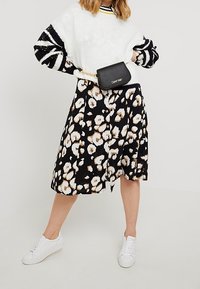 Sort nederdel med hvidt blomsterprint, kombineret med en hvid sweater med sorte og marineblå striber. Hvide sneakers og en lille sort taske.