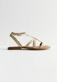 Beige platta sandals med flera remmar och guld färgad hårdvara. Har en T-formad design och en dämpad sula för komfort.