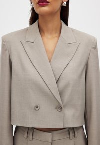 Cropped double-breasted blazer in light gray fabric with a smooth texture. Features pointed lapels and two button closures.