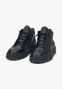 Czarne skórzane botki za kostkę z teksturowaną gumową podeszwą, z zamkiem błyskawicznym z przodu, okrągłym noskiem i przeszyciami.