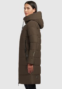 Manteau en duvet marron avec capuche, présentant un design matelassé, des zips sur les côtés et un logo accentué sur le bas à l'avant. Texture lisse et mate.