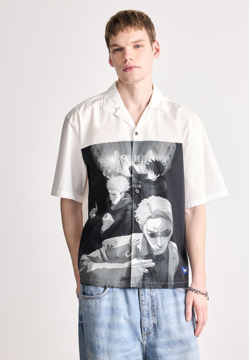 Κοντομάνικη πουκάμισο με κουμπιά σε λευκό και μαύρο χρώμα, με εικονογραφημένα γραφικά που απεικονίζουν χαρακτήρες. Φτιαγμένο από ελαφρύ ύφασμα, με χαλαρή εφαρμογή.