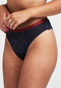 Lingerie blu navy con dettagli in pizzo floreale, centro in rete trasparente e una fascia elastica bordeaux, con bordi ondulati.
