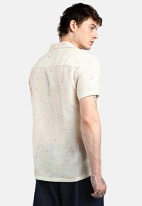Camicetta in lino beige con maniche corte e motivi astratti colorati a macchie. Presenta un colletto e un orlo dritto.