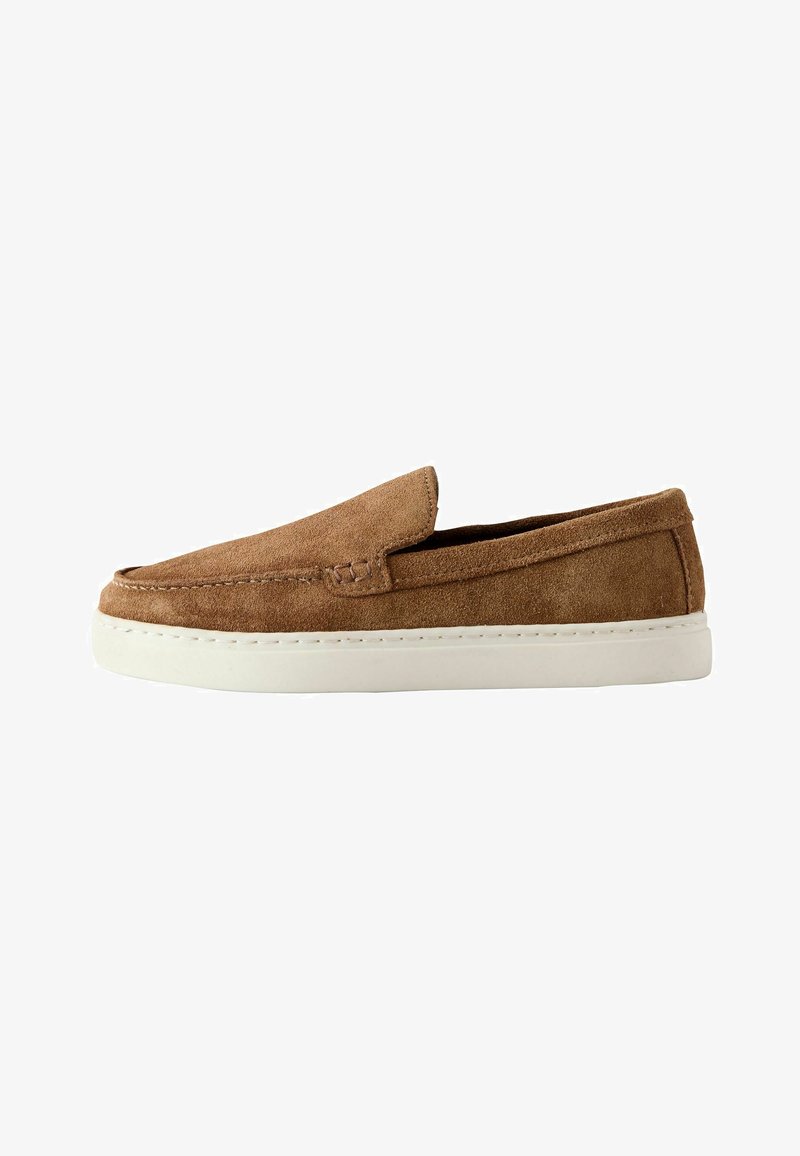 Zapato de ante marrón sin cordones con suela de goma blanca, punta redonda y detalles de costura a lo largo del borde superior.