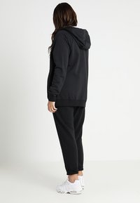 Svart hoodie med lång ärm och känguruficka, kombinerad med matchande sweatpants. Båda plaggen har en avslappnad passform och en mjuk textur.