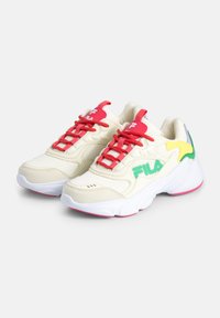 Baskets de couleur crème avec des lacets rouges, en tissu en maille, avec des accents verts et jaunes, et une semelle blanche dotée d'un liseré rose. Logo Fila affiché.