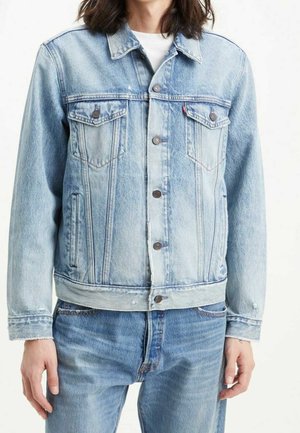 Person wearing light blue denim jacket with button closure, chest flap pockets, paired with matching blue jeans and white undershirt.