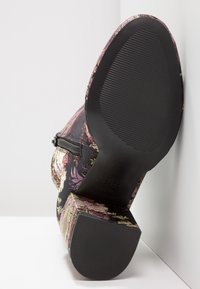 Bottine noire à motif floral avec un tissu ornemental aux nuances de rose et d'or. Détail zip notable et semelle en caoutchouc texturée.