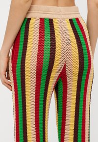 Gestrickte Schlaghosen mit einem Netzdesign, das vertikale Streifen in Rot, Grün, Gelb, Braun und Beige zeigt. Elastischer Bund sichtbar.