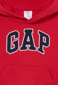 Röd barnhoodie med marinblå "GAP"-bokstäver i vitt och en framficka i kangaroo-stil.