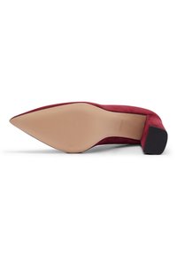 Chaussure à talon haut en daim rouge avec un bout pointu, une semelle texturée beige et un talon bloc noir, présentant un design élégant et moderne.