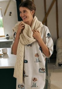Loungewear in cotone grigio chiaro con stampe di cani, abbinato a una sciarpa in maglia spessa di colore crema con un motivo testurizzato.