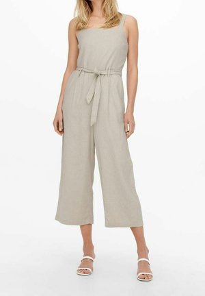 Lysebeige buksedragt med firkantet udskæring, vide ben og et stofbælte. Fremstillet af et struktureret materiale og med tynde stropper.