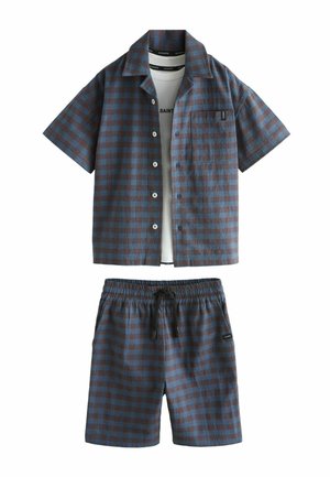 Blau-braun kariertes Kurzarmhemd mit Knöpfen, passenden Shorts und teilweise sichtbarem weißen T-Shirt darunter.