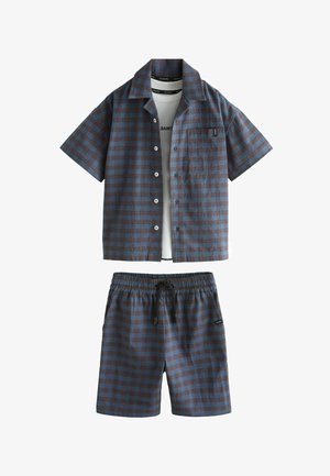 Blå og brun ternet kortærmet skjorte med knapper med matchende shorts og delvist synlig hvid T-shirt under.