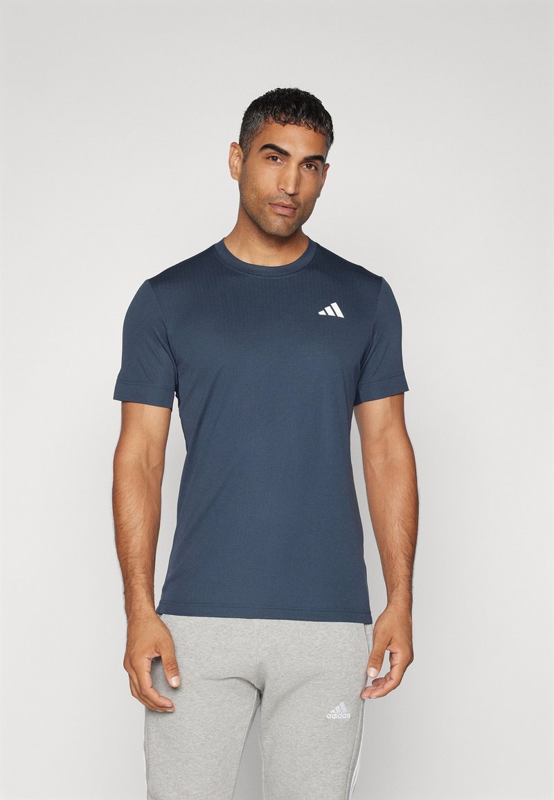 Camiseta atlética de manga corta de color azul marino con cuello redondo y un logotipo de tres franjas blancas en el área del pecho izquierdo. Textura suave.