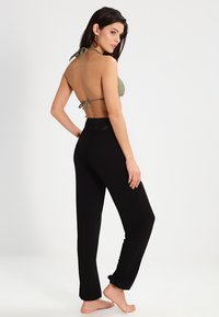 Top de bikini de halter verde oliva combinado con pantalones negros holgados que cuentan con una cintura elástica y un diseño texturizado.