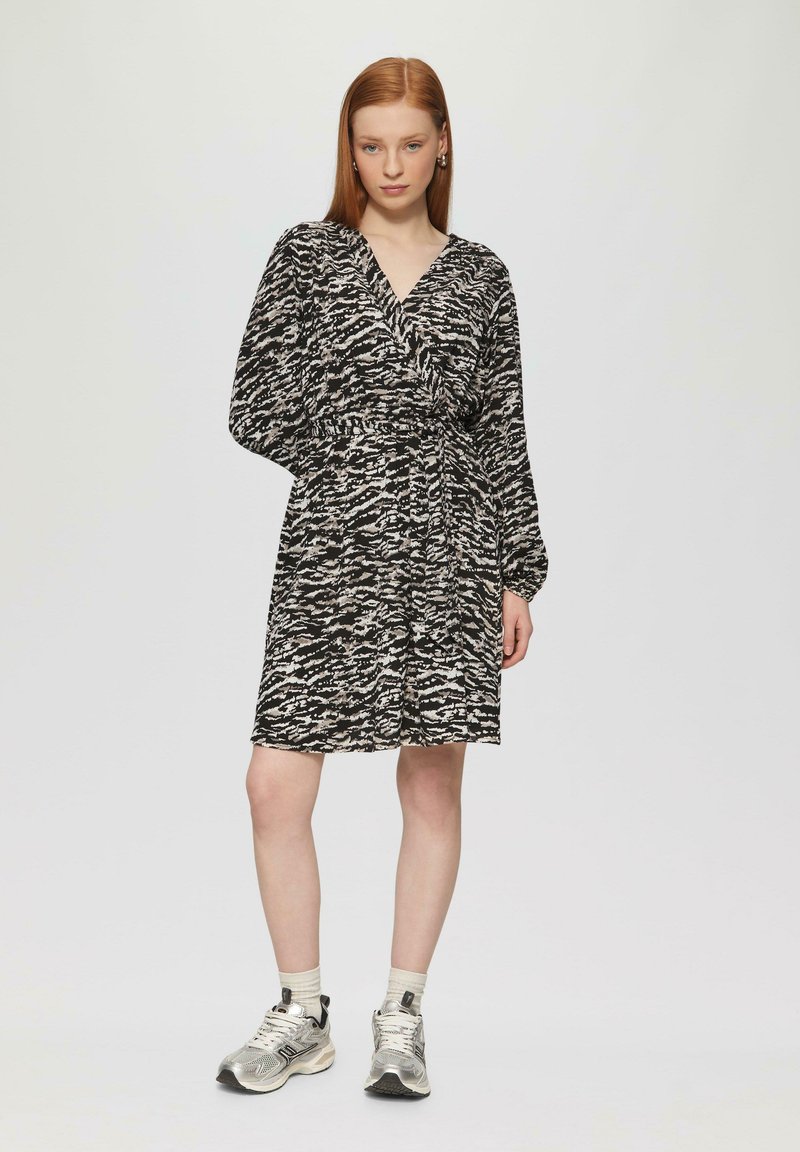 Abito a pois bianco e nero con scollo a V, vita elastica e maniche lunghe, abbinato a scarpe sportive metalliche e calzini alla caviglia.