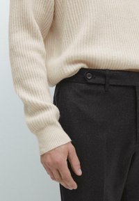 Beige ribbad tröja i kombination med mörkgrå skräddarsydda byxor. Tröjan har en lös passform; byxorna har en knappstängning och en strukturerad design.