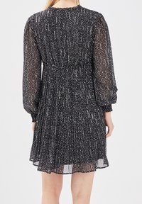 Robe noire avec une texture transparente, ornée d'un motif tacheté blanc. Manches longues et bouffantes, ainsi qu'une taille froncée, conçue pour se mouvoir doucement.