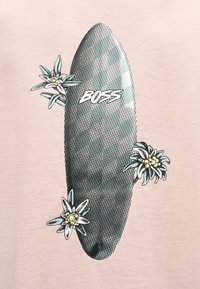 Κάθετη ασπρόμαυρη σανίδα για σέρφ με πουά μοτίβο, τη λέξη «BOSS» και τρία λευκά και κίτρινα λουλούδια σε ανοιχτό ροζ φόντο.