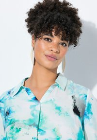 Camicia leggera con scollatura a V, caratterizzata da una stampa floreale ad acquerello in tonalità di blu e verde. Il modello indossa grandi orecchini metallici.