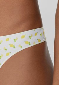 Białe majtki bikini z motywem cytryn, zdobione żółtymi cytrynami i zielonymi liśćmi. Gładki materiał, niski krój i elastyczny pas.