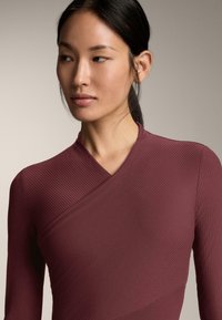 Bordó hosszú ujjú felső átfedős kialakítással, bordázott textúrával és v-nyakkal. A szövet sima és enyhén fényes hatású.