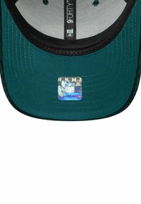 Türi Baseballkappe mit schwarzem Schirm, ausgestattet mit einem holografischen NFL-Logosticker auf der Unterseite. Glattes Gewebe mit sichtbaren Nähten.