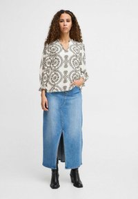 Hvid bluse med sort mønsterdesign og en blå denim maxiskirt med en frontslids, parret med sorte stiletter.