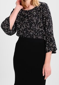 Black floral blouse with three-quarter bell sleeves and a round neckline, featuring small pink and white flower patterns. Paired with a black skirt.