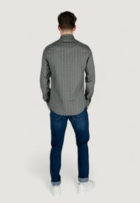 Camicia a bottoni grigia con motivo, colletto, maniche lunghe e taglio dritto. Indossata con jeans blu scuro e sneakers bianche.