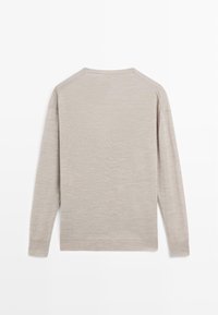 Pull-over à manches longues beige clair avec une texture lisse. Il présente un col rond et des poignets côtelés, offrant une coupe décontractée.