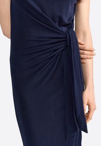 Vestido azul marino confeccionado en una tela suave, con un diseño retorcido en la cintura que incluye un lazo y una textura lisa y minimalista.