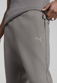 Sive trenirke od mekog materijala, s blagom teksturom, bočnim džepovima i malim reflektirajućim Puma logom.