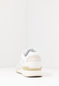 Sneaker bianca con accenti beige e sottili cuciture blu. Presenta una punta arrotondata, colletto imbottito e suola in gomma testurizzata per una maggiore aderenza.