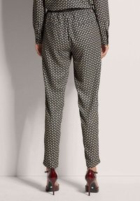 Zwarte broek met een diamanten patroon, elastische tailleband en omgeslagen broekspijpen. Draagt het met bordeauxrode hoge hakken.