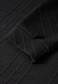 Tissu noir texturé avec un motif en grille, présentant un pli superposé montrant une surface subtilement côtelée.