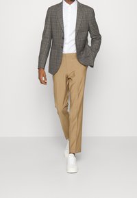 Grau karierter Blazer, weißes Button-Up-Hemd, beige Hose und weiße Sneaker. Maßgeschneiderte Passform, glatte Stoffe und klare Linien.