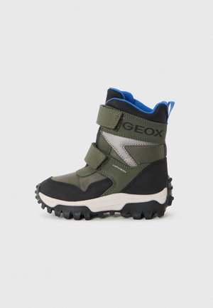 Bottes pour enfants vertes et noires avec une finition texturée, dotées de deux bandes Velcro et d'une semelle robuste pour une meilleure adhérence. Doublure bleue et logo visibles.