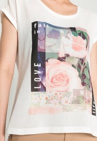 White cotton t-shirt with a relaxed fit, featuring a floral graphic design in shades of pink and green, accented by black text elements.