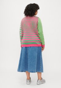 Knit sweater in pink and green patterns, featuring spiral and zigzag designs. Paired with a denim A-line skirt and grey sneakers.