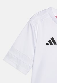 Maillot Adidas blanc avec manches courtes, trois bandes sur les épaules et un logo noir imprimé sur le devant. Texture de tissu lisse.