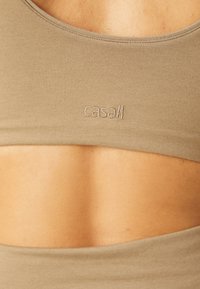 Khaki sports bra made of soft fabric with a rounded neckline and cut-out back. Features embroidered "casall" logo near the hem.
